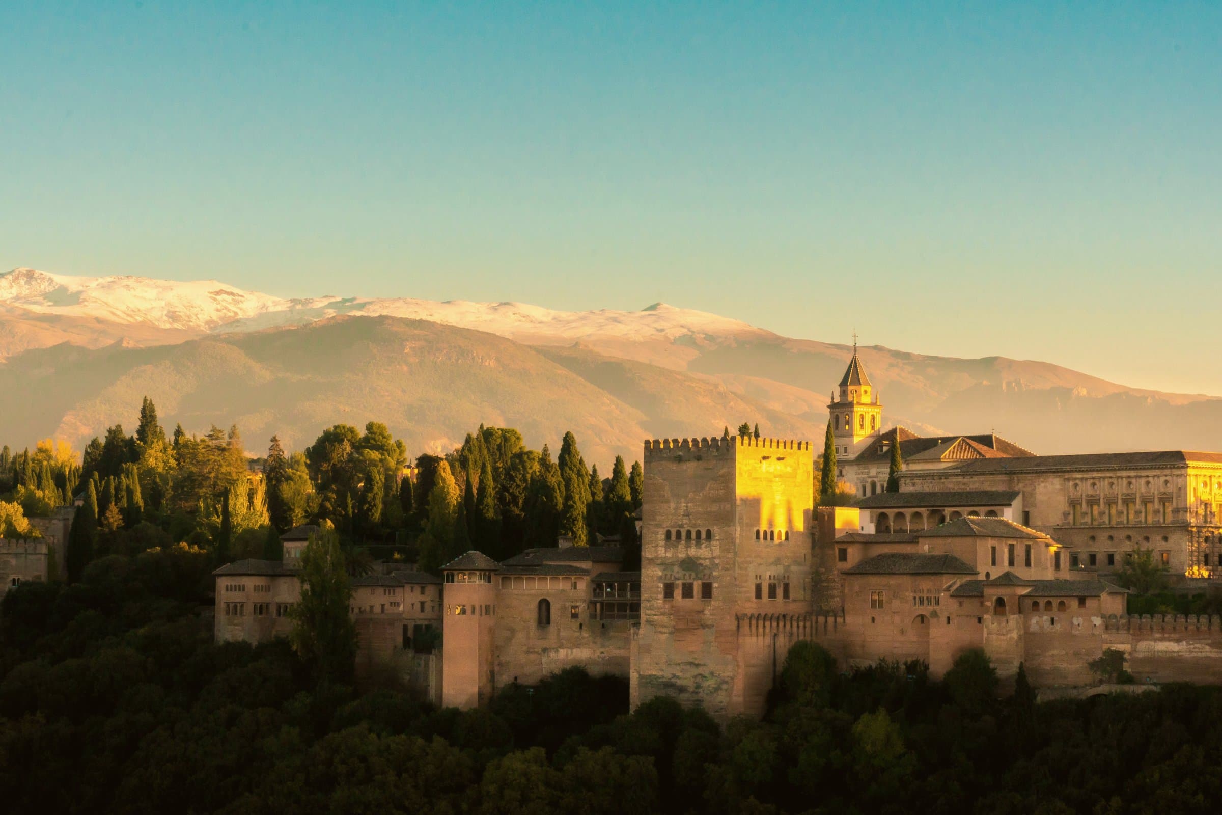 The Alhambra palace and fortress in Granada at sunset, with the snow-capped Sierra Nevada mountains behind, Spain
