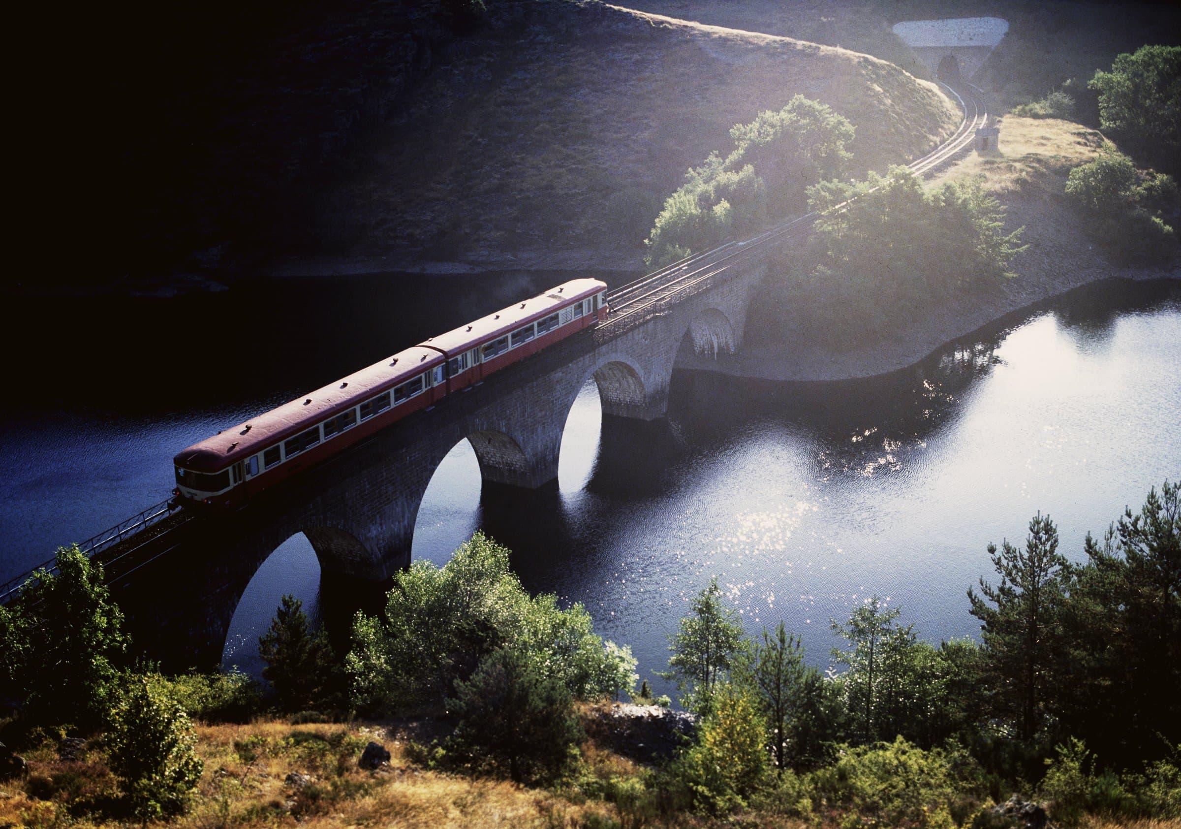 A red regional train crossing a stone viaduct on the Cévennes line, southern France