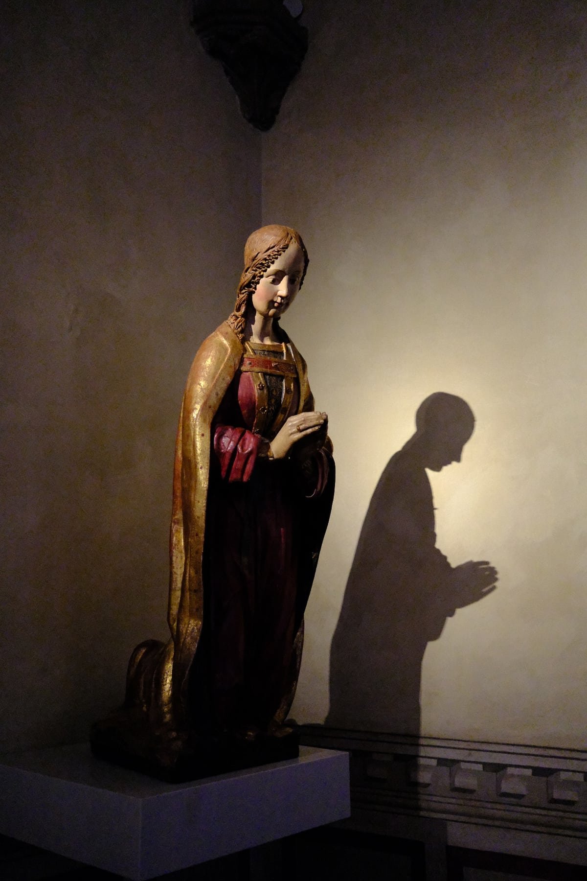 A gilded wooden figure of a praying woman in the Bargello, her shadow cast on the wall