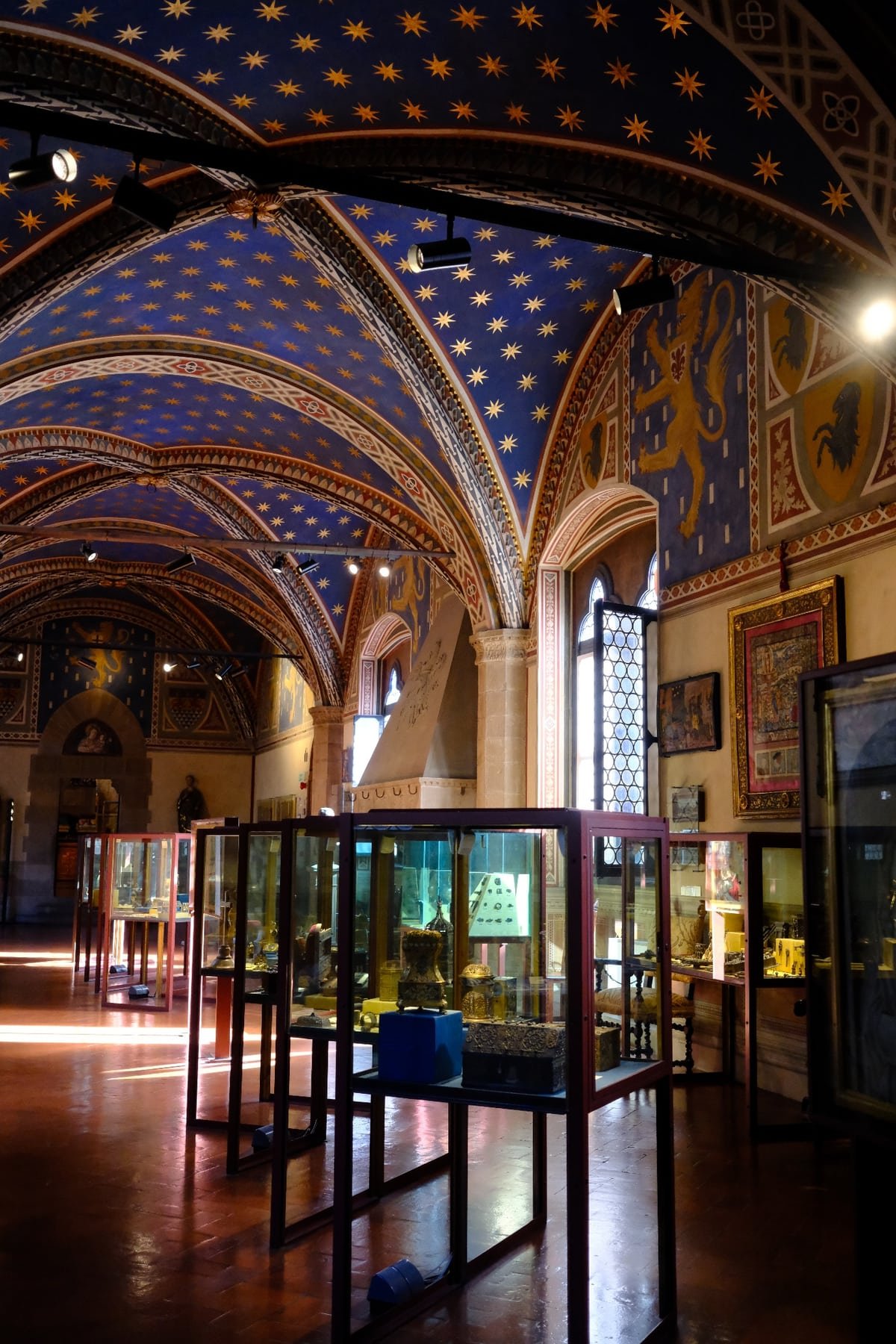 A gallery in the Bargello beneath a blue vault painted with gold stars and lions