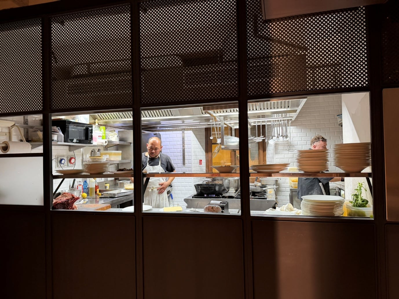 Chefs working in the kitchen of Vini e Vecchi Sapori, seen through a metal screen