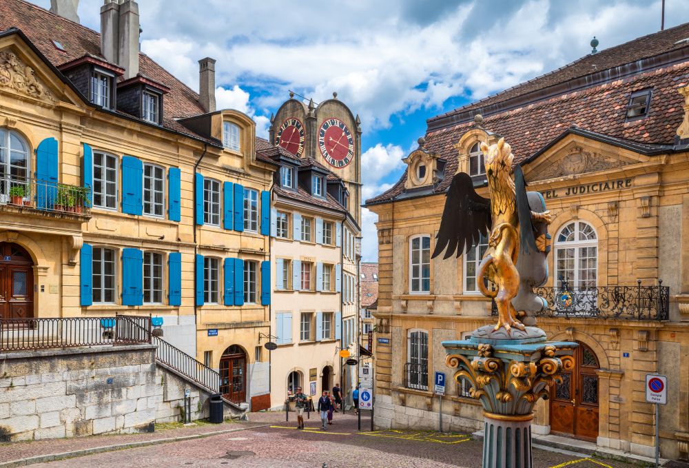 A gilded griffin on a column in Neuchâtel's old town, among yellow limestone houses and a clock tower